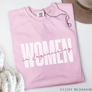 May include: A pink t-shirt with the text "Women in Engineering" in white letters. The text is in a bold, blocky font. The shirt is made of a soft, comfortable material.