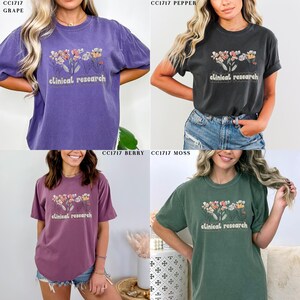 May include: Four different colored t-shirts with a floral design and the text "clinical research". The colors are grape, pepper, berry, and moss.