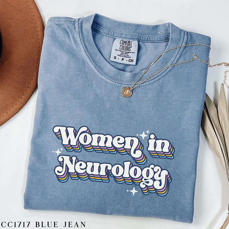 May include: A blue jean t-shirt with the text "Women in Neurology" in a retro rainbow font. The text is surrounded by small white stars.