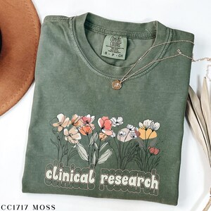 May include: A green t-shirt with a floral design and the text "clinical research" in a retro font. The shirt is made of a soft, comfortable material and is perfect for everyday wear.
