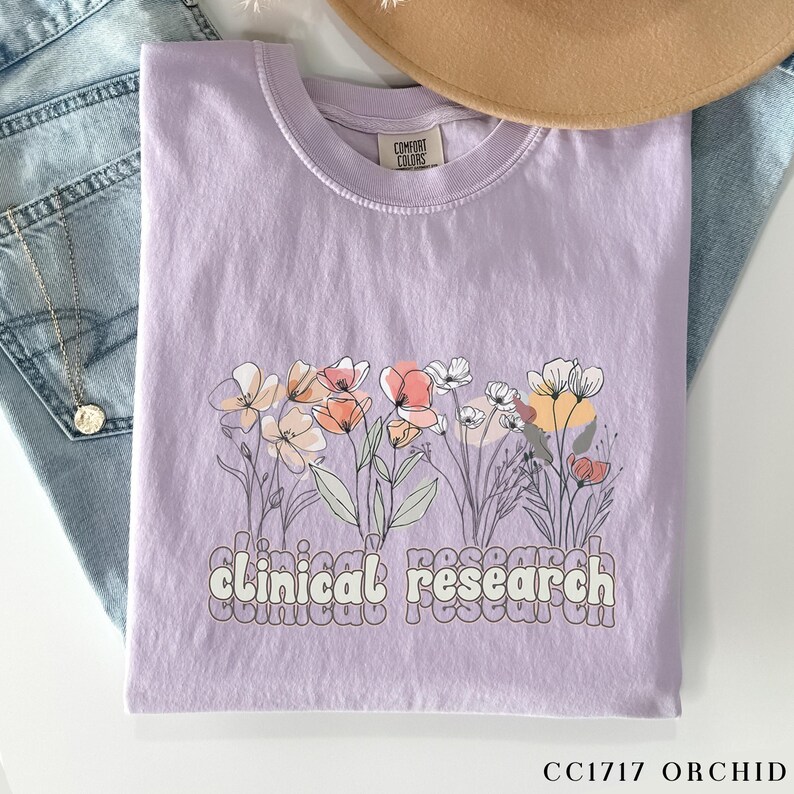 May include: A lavender t-shirt with a floral design and the text "clinical research" in a retro font.