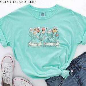 May include: A light blue t-shirt with a floral design and the text "clinical research" in a retro font.