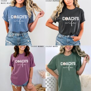 Może przedstawiać: Cztery r&oacute;żne kolory koszulek z napisem "COACH'S wife" i grafiką baseballa. Koszulki są w kolorze niebieskim, pieprzowym, jagodowym i mchu.