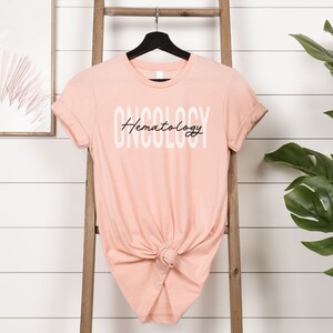 May include: A peach-colored t-shirt with the text "ONCOLOGY Hematology" printed in white on the front.
