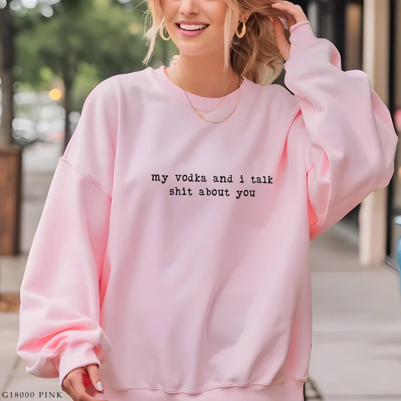 May include: A pale pink sweatshirt featuring the black text "my vodka and i talk shit about you". The top has a crew neck and long sleeves.