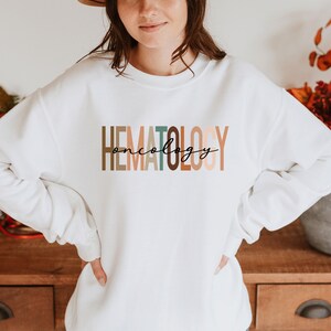May include: White sweatshirt with the text "HEMATOLOGY oncology" in colorful, stacked letters.