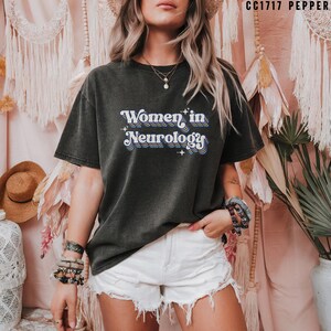 May include: A dark gray t-shirt with the text "Women in Neurology" in a retro rainbow font.