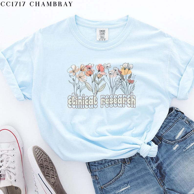 May include: Light blue t-shirt with a floral design and the text "clinical research" in a retro font.