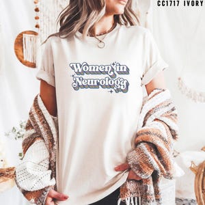 May include: A white t-shirt with the text "Women in Neurology" in a retro rainbow font.