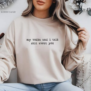 May include: A sand-coloured sweatshirt featuring the black text "my vodka and i talk shit about you". The long-sleeved crew neck top is a neutral colour and has a relaxed fit.