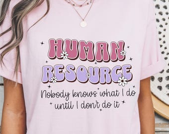 May include: Pink t-shirt with the text "HUMAN RESOURCE" in a retro font with flowers and stars. The text "Nobody knows what I do until I don't do it" is below the main text.