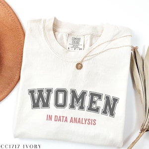 May include: Ivory t-shirt with the text "WOMEN IN DATA ANALYSIS" in a collegiate font. The text "WOMEN" is in gray and "IN DATA ANALYSIS" is in pink.