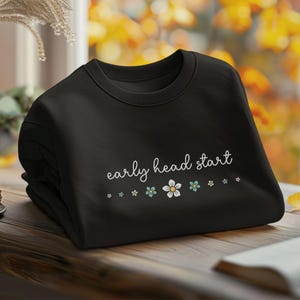 May include: Black sweatshirt with the text "early head start" in white cursive lettering. A row of small blue and white flowers are below the text.