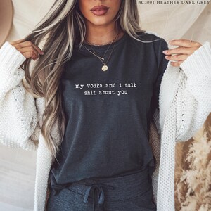 May include: Dark grey heather t-shirt featuring the white text "my vodka and I talk shit about you". The top is a crew neck style.