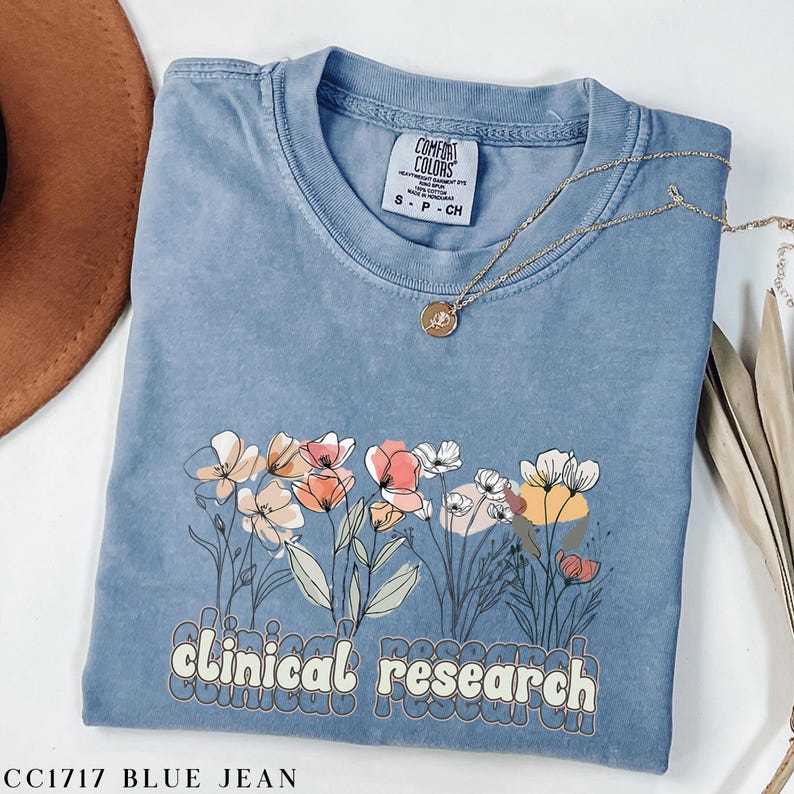 May include: A light blue t-shirt with a floral design and the text "clinical research" in a retro font. The shirt is made of a soft, comfortable material and has a relaxed fit.