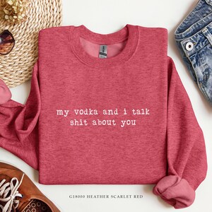 May include: Heather scarlet red sweatshirt with the text "my vodka and i talk shit about you" in white. The sweatshirt is a crew neck style and has long sleeves. The bottom of the sweatshirt has a rolled hem.