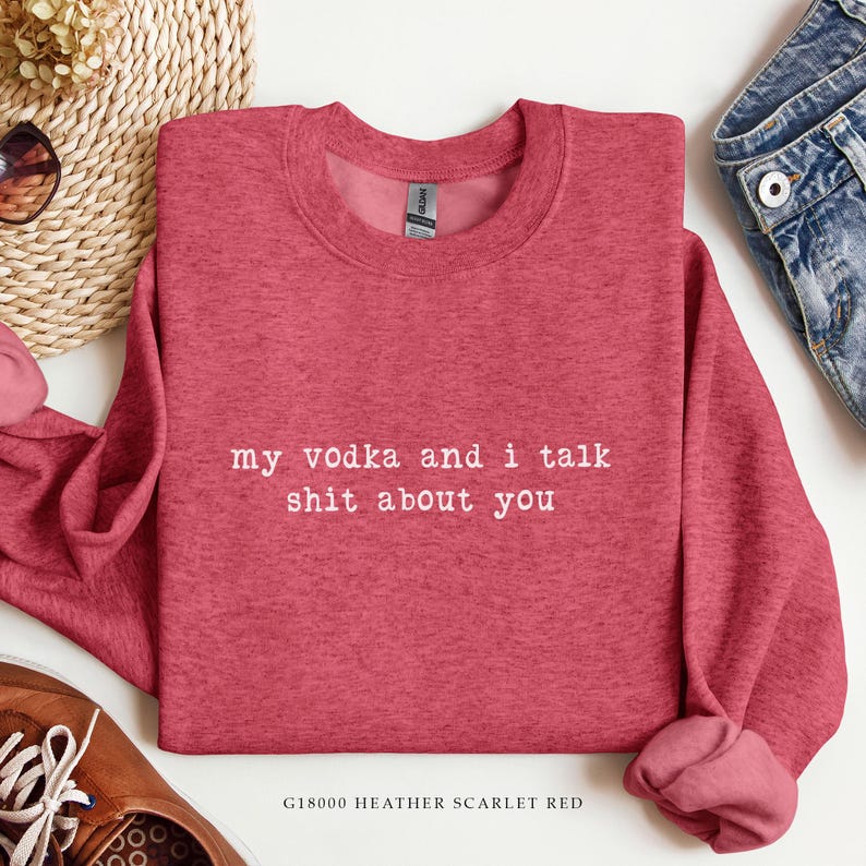 May include: Heather scarlet red sweatshirt with the text "my vodka and i talk shit about you" in white. The sweatshirt is a crew neck style and has long sleeves. The bottom of the sweatshirt has a rolled hem.