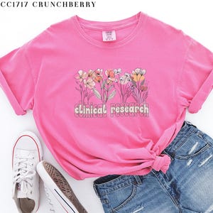 May include: Pink t-shirt with a floral design and the text "clinical research" in a retro font.