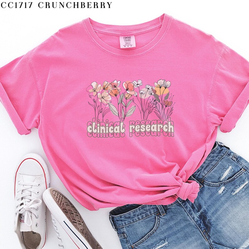 May include: Pink t-shirt with a floral design and the text "clinical research" in a retro font.