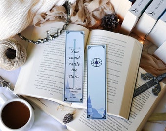 May include: Two bookmarks with a blue and white design. One bookmark features a sword and the quote "You could rattle the stars." from the book "Throne of Glass" by Sarah J. Maas. The other bookmark features a blue eye symbol.
