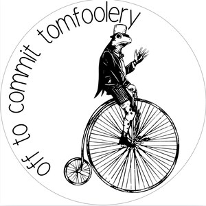 May include: Black and white illustration of a frog in a top hat and suit riding a penny-farthing bicycle. The text "off to commit tomfoolery" is written around the edge of the circle.