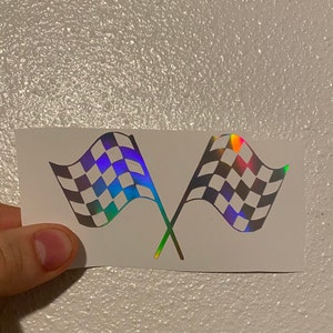 May include: A white sticker with two iridescent checkered flags crossed over each other. The flags have a rainbow sheen.