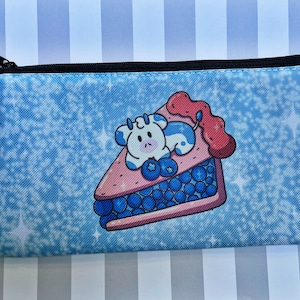 May include: A blue and white canvas zippered pouch with a cartoon cow on a blueberry pie. The pouch has a sparkly blue background.