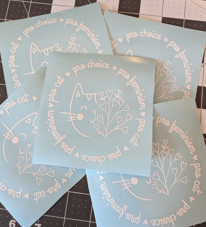 May include: Four light blue vinyl stickers with a white cat design and the text "pro cat pro choice pro feminism".