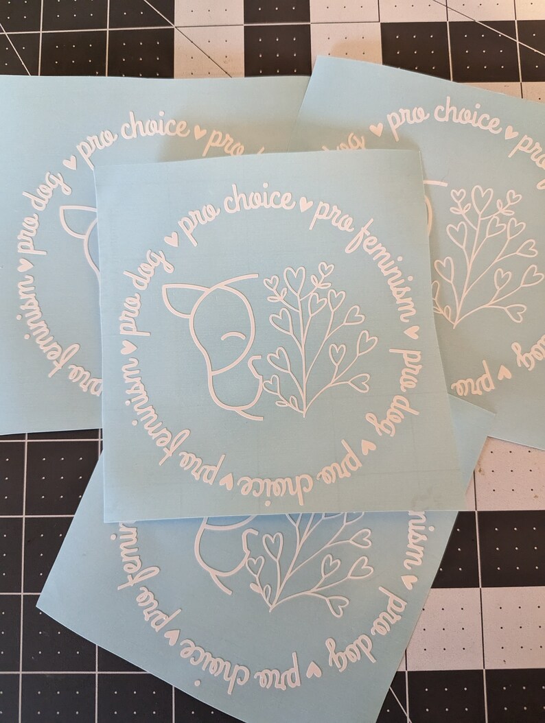 May include: Three blue vinyl stickers with white text and a white outline of a dog with a heart-shaped flower. The text on the stickers reads "pro dog pro choice pro feminism".