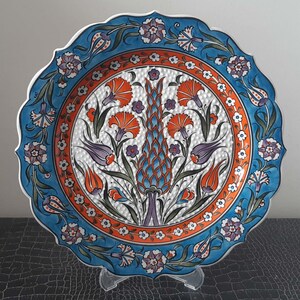 Pode incluir: Um prato de cer&acirc;mica branco com um design floral azul e laranja. O prato tem uma borda festonada e &eacute; decorado com um padr&atilde;o repetitivo de flores e folhas.