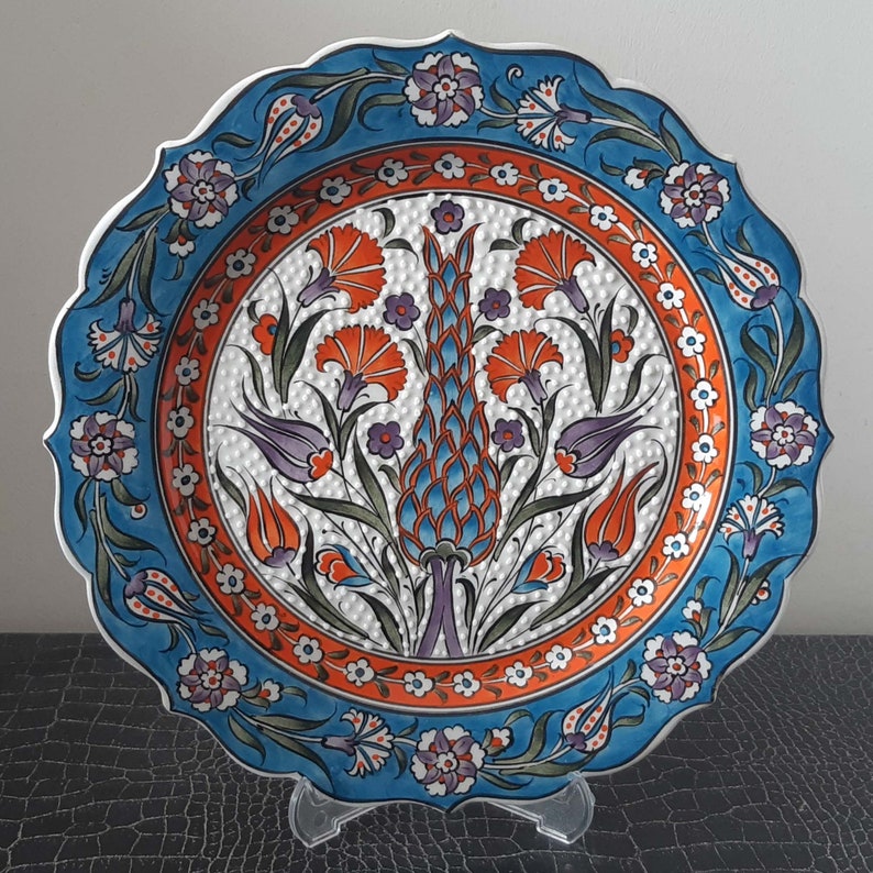 Pode incluir: Um prato de cer&acirc;mica branco com um design floral azul e laranja. O prato tem uma borda festonada e &eacute; decorado com um padr&atilde;o repetitivo de flores e folhas.