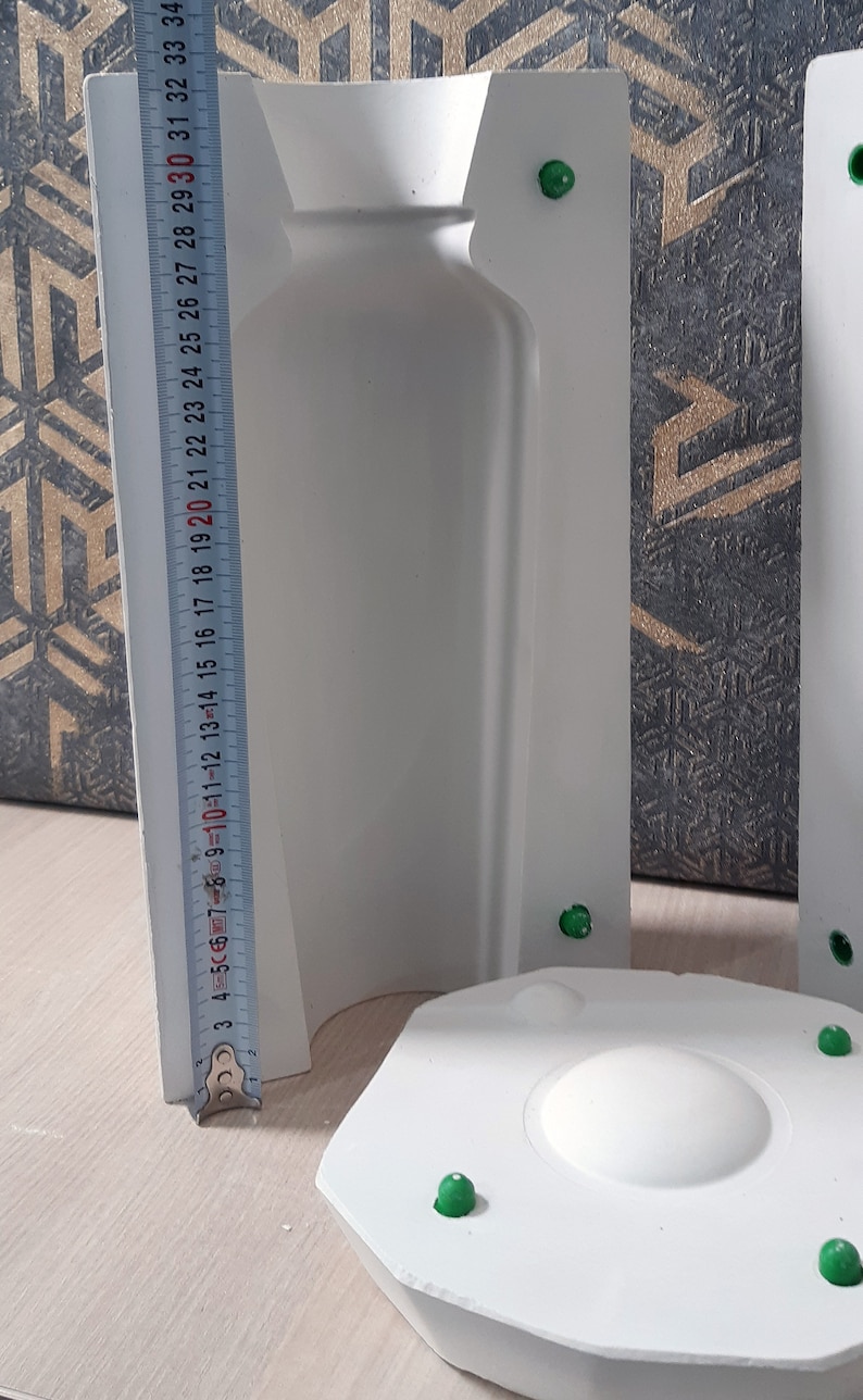 May include: White plaster mold for making a bottle shaped candle. The mold is 30 inches tall and has a round base. The mold is made in two pieces, with a top and bottom section. The mold is designed to create a bottle shaped candle with a smooth, even surface.