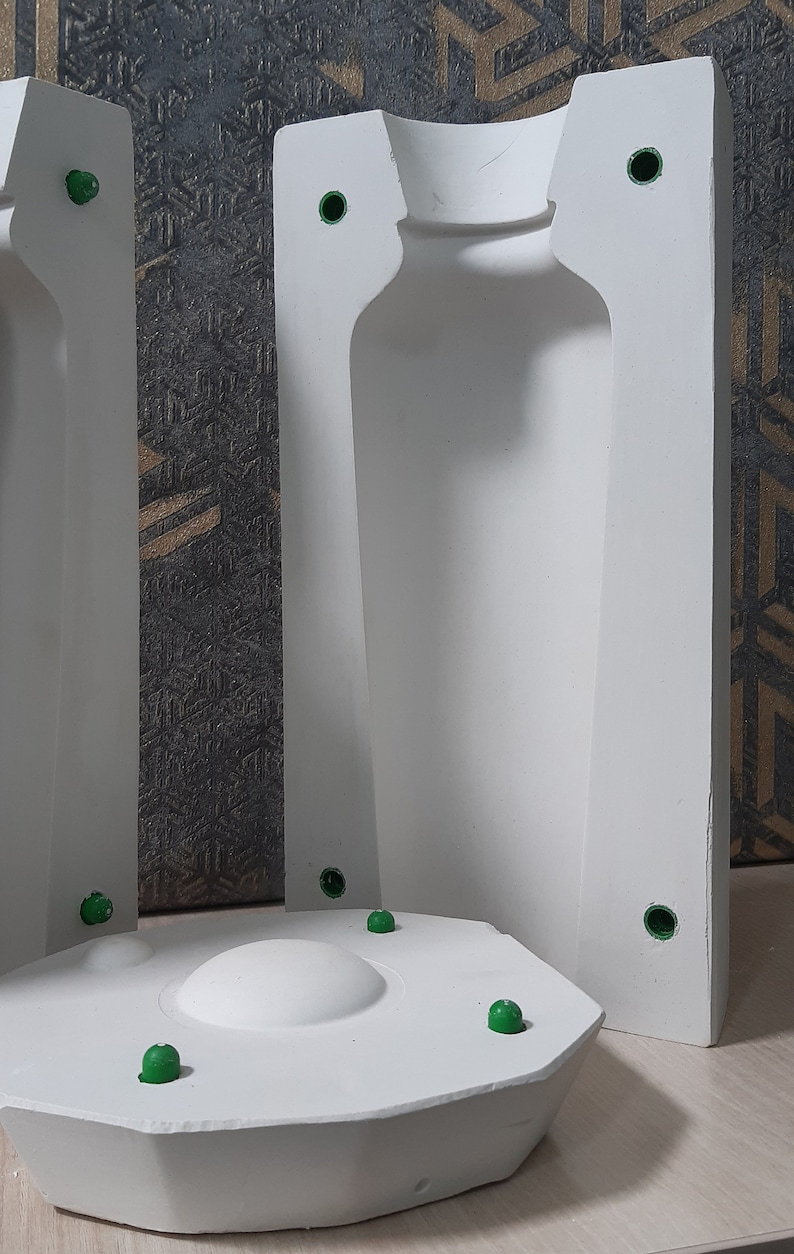 May include: Two white plaster molds for making a bottle. The molds are open on one side and have a round base. The molds have green plastic plugs in the sides.