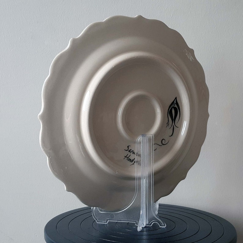 Pode incluir: Prato de cer&acirc;mica branco com borda ondulada. A parte de tr&aacute;s do prato tem um desenho preto e as palavras "Serve Hand Painted".