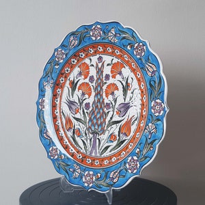 Pode incluir: Um prato de cer&acirc;mica branca com um desenho floral azul e laranja. O prato tem uma borda ondulada e &eacute; decorado com um padr&atilde;o turco tradicional.