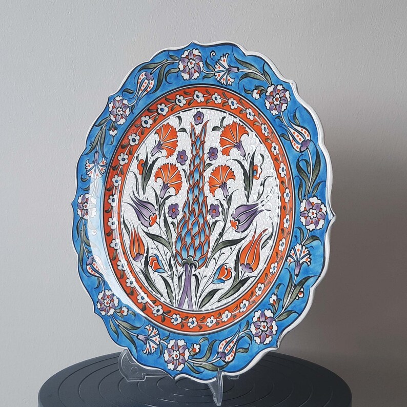 Pode incluir: Um prato de cer&acirc;mica branca com um desenho floral azul e laranja. O prato tem uma borda ondulada e &eacute; decorado com um padr&atilde;o turco tradicional.