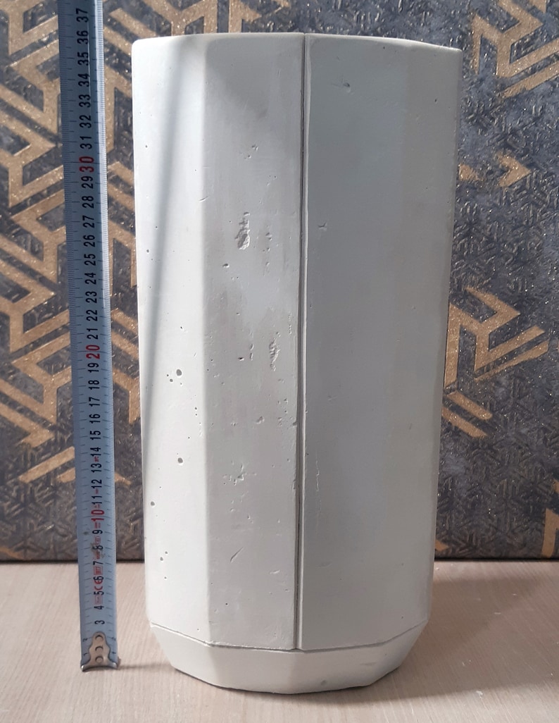 May include: A white concrete planter with an octagonal shape and a smooth, textured surface. The planter is approximately 37 inches tall.