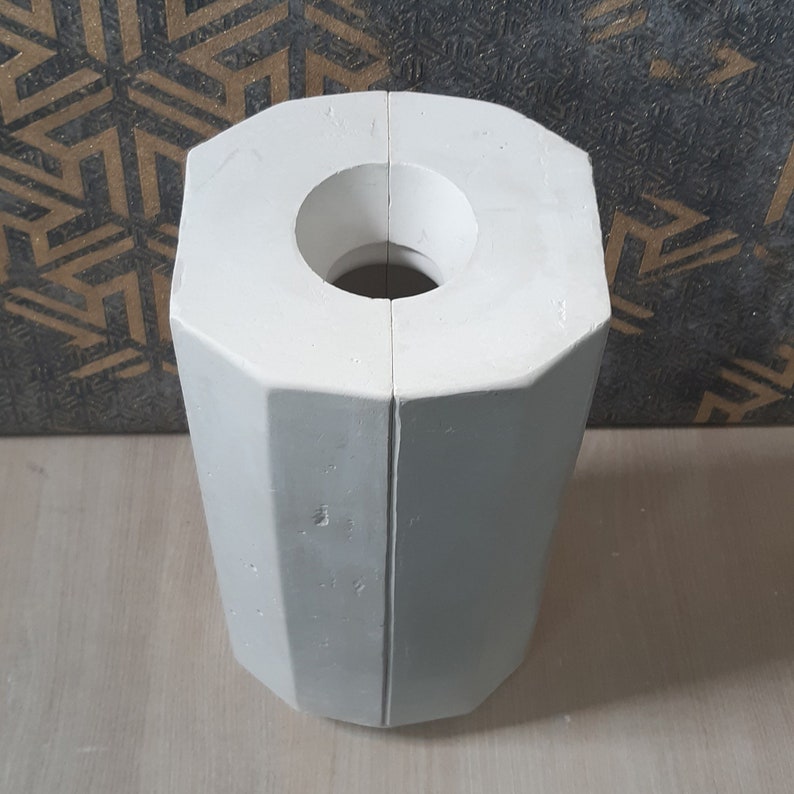 May include: A white, two-piece, octagonal mold for making candles. The mold is split in half and has a round hole in the center.