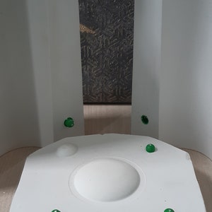 May include: A white, circular, raised platform with a smooth, rounded top. Four green dots are attached to the platform's edge.