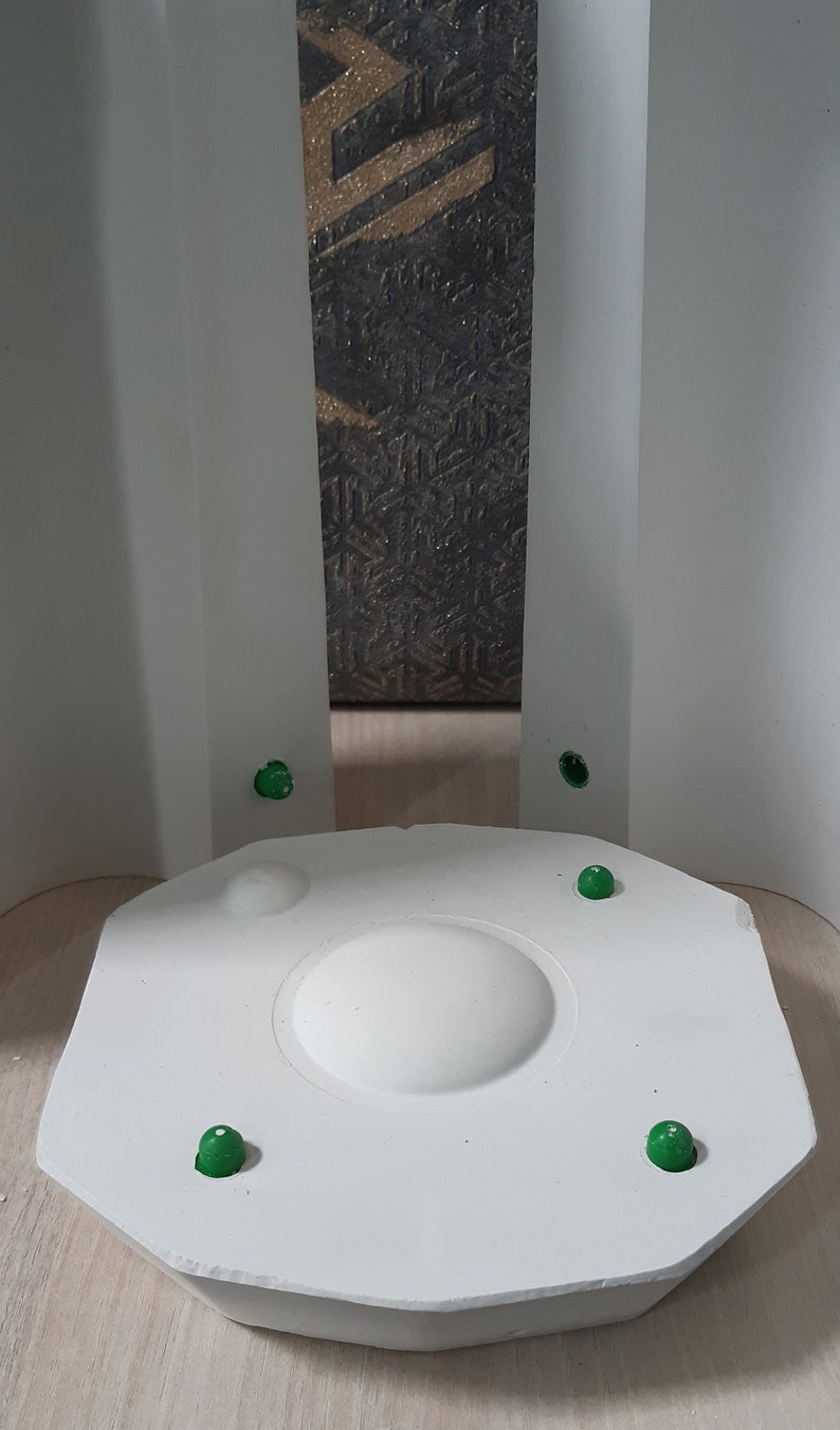 May include: A white, circular, raised platform with a smooth, rounded top. Four green dots are attached to the platform's edge.