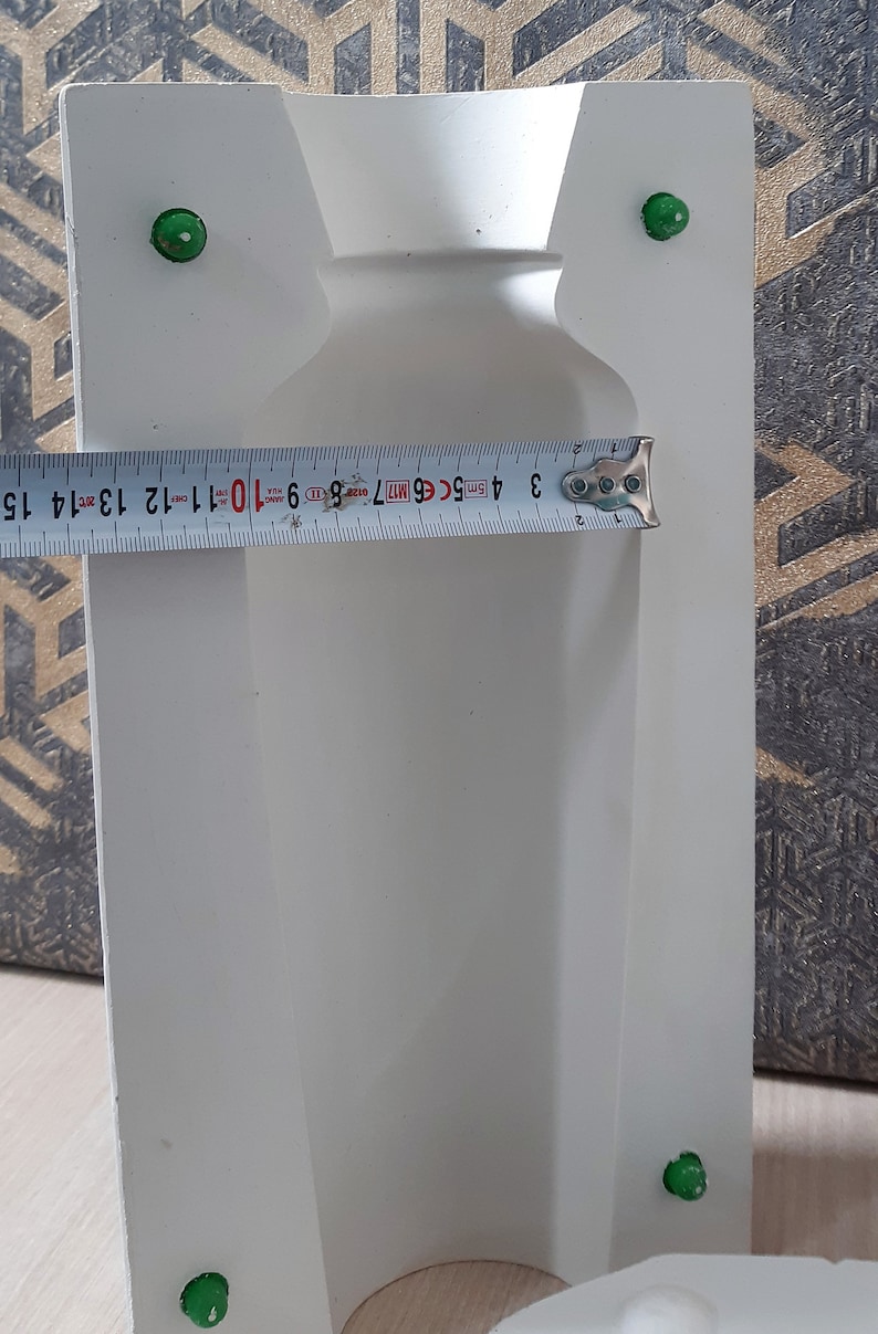 May include: White plaster mold for making a vase. The mold is 15 inches tall and has a round opening at the top. There are four green plastic stoppers on the mold.