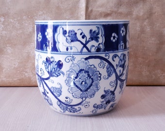 May include: A white ceramic planter with a blue and white floral design. The planter has a rounded shape and a wide opening.