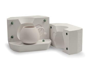 May include: Two-piece white plaster mold for making a ceramic mug. The mold is open and a white ceramic mug is inside the mold.