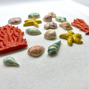 Puede incluir: Una colecci&oacute;n de encantos de cer&aacute;mica de vida marina, que incluyen coral, estrellas de mar, conchas marinas y una concha de caracol. Los encantos est&aacute;n pintados en varios tonos de azul, verde, amarillo, naranja y rosa.