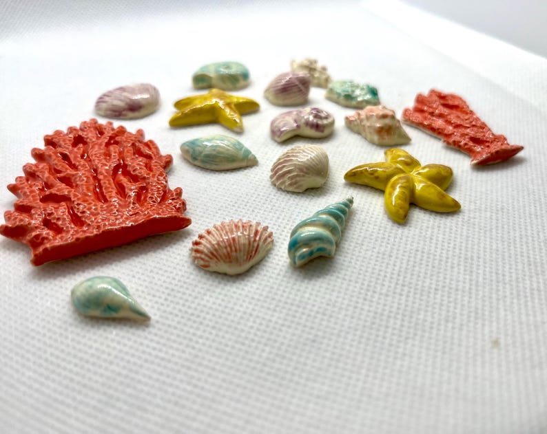 Puede incluir: Una colecci&oacute;n de encantos de cer&aacute;mica de vida marina, que incluyen coral, estrellas de mar, conchas marinas y una concha de caracol. Los encantos est&aacute;n pintados en varios tonos de azul, verde, amarillo, naranja y rosa.