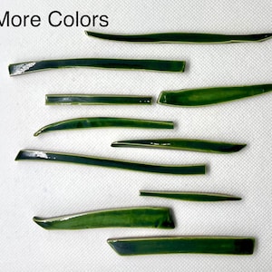 May include: A collection of ten green ceramic tiles in various shapes and sizes. The tiles are arranged in a random pattern on a white surface. The text "More Colors" is written in black at the top of the image.