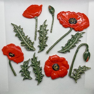 May include: A collection of ceramic poppy flower components including three full red blossoms with black centers, one closed bud, one partially open bud on a stem, and six individual green serrated leaves with a glossy finish.