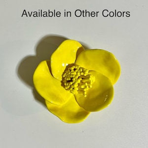 May include: A bright yellow ceramic flower with five petals. The flower has a textured center.