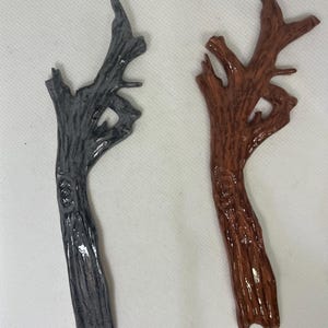 Peut inclure: Deux sculptures décoratives en forme de branches d'arbre. L'une est peinte en gris foncé, l'autre en marron brillant. Les deux ont un aspect texturé, semblable à de l'écorce, et sont conçues avec de multiples ramifications.