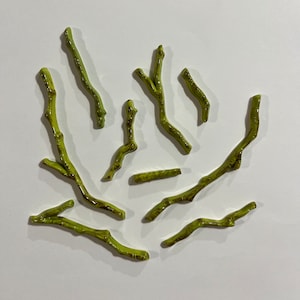 May include: A collection of nine green ceramic twig-shaped ornaments. The twigs are arranged in a loose, organic pattern.